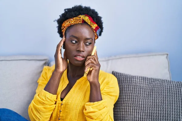 年轻的非洲裔美国女人坐在家里的沙发上用智能手机聊天 — 图库照片