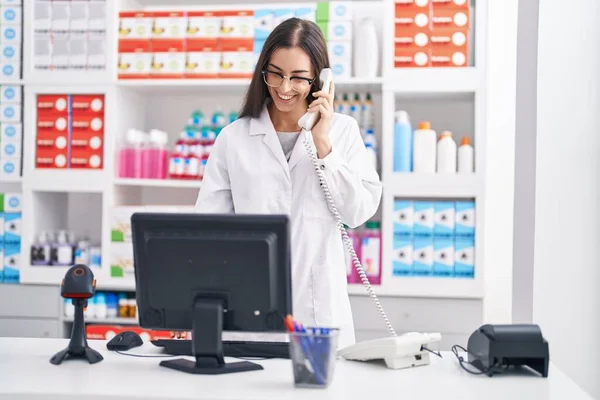Young Beautiful Hispanic Woman Pharmacist Talking Telephone Using Computer Pharmacy — Foto Stock