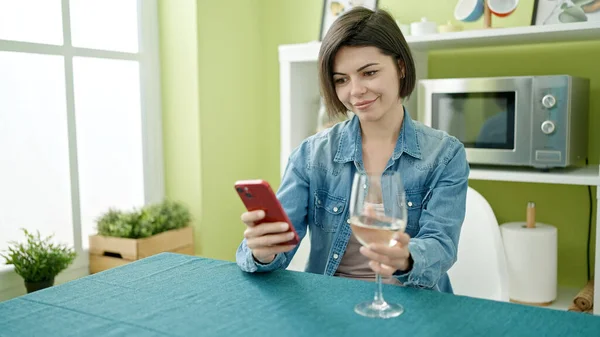 Jonge Kaukasische Vrouw Met Behulp Van Smartphone Drinken Wijn Thuis — Stockfoto