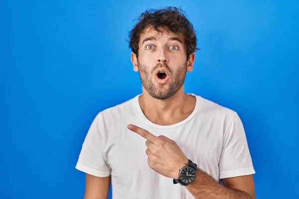 Hispanic Young Man Standing Blue Background Surprised Pointing Finger Side — Stock Fotó