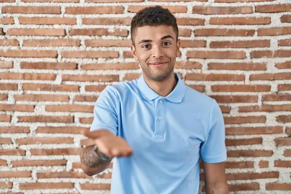 ブラジルの若い男がレンガの壁の上に立って笑顔陽気な提供ヤシの手援助と受け入れ — ストック写真