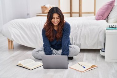 Young hispanic woman sitting on floor studying at bedroom