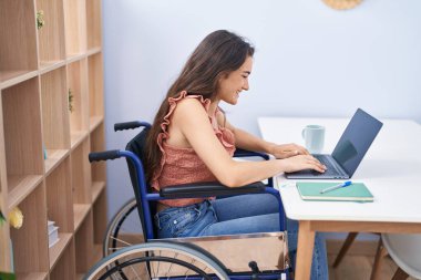Young hispanic woman sitting on wheelchair studying at home