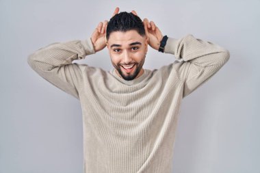 Soyutlanmış arka planda duran genç ve yakışıklı bir adam komik ve çılgın poz veriyor parmakları kafasında tavşan kulakları, neşeli bir gülümseme 