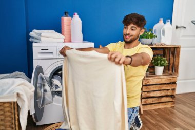 Young arab man holding sweater washing clothes at laundry room