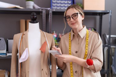 Genç Kafkas kadın terzi defterine yazı yazıyor. Atölyede manikinin yanında.