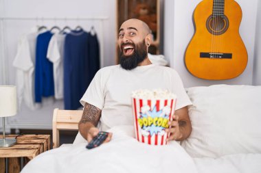 Sakallı ve dövmeli genç İspanyol adam yatakta patlamış mısır yiyor. Çılgınlığı kutluyor ve başarıyı hayretle izliyor. Heyecanlı çığlıklar atıyor.. 