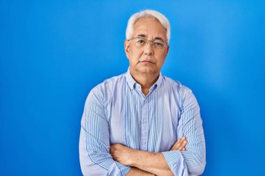 Hispanic senior man wearing glasses skeptic and nervous, disapproving expression on face with crossed arms. negative person. 