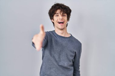 İzole edilmiş arka planda duran genç adam dostça bir selamlama ve hoş geldin hediyesi olarak el sıkışmayı sunuyor. başarılı iş. 