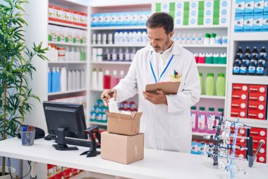 Middle age man pharmacist holding pills bottle reading paperwork at pharmacy