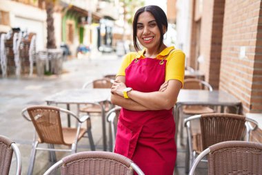 Young beautiful arab woman waitress smiling confident standing with arms crossed gesture at coffee shop terrace