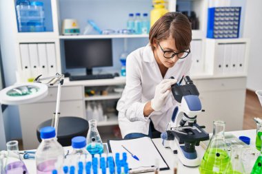 Laboratuvarda mikroskop kullanan genç ve güzel İspanyol bilim kadını.