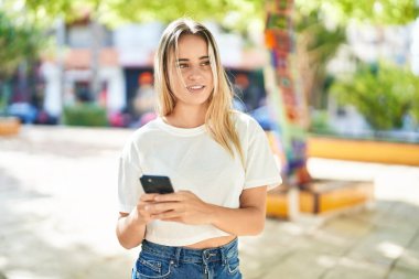 Parkta akıllı telefon kullanan, kendine güvenen genç sarışın kadın.