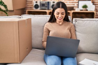 Young beautiful hispanic woman smiling confident using laptop at new home