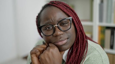 Saçları örgülü Afrikalı kadın üniversite kütüphanesinde düşünüyor.