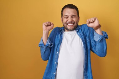 Sarı arka planda duran İspanyol adam başarı için heyecanlanıyor kolları havada ve gözleri kapalı zaferi kutlarken gülümsüyor. Kazanan konsept. 