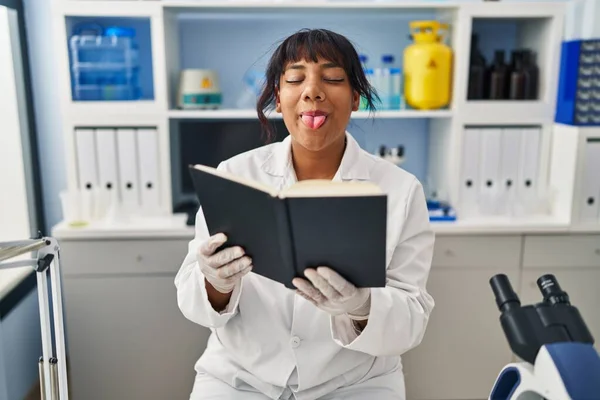 Hispanic Woman Working Scientist Laboratory Reading Book Sticking Tongue Out — Stock Photo, Image