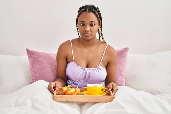 头戴辫子的非洲裔美国女人拿着托盘 床上有早餐吃 她的思维 态度和严肃的表情看上去很自信 — 图库照片