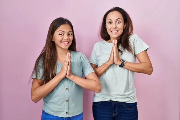 Young Mother Daughter Standing Pink Background Praying Hands Together Asking — Stock Photo, Image