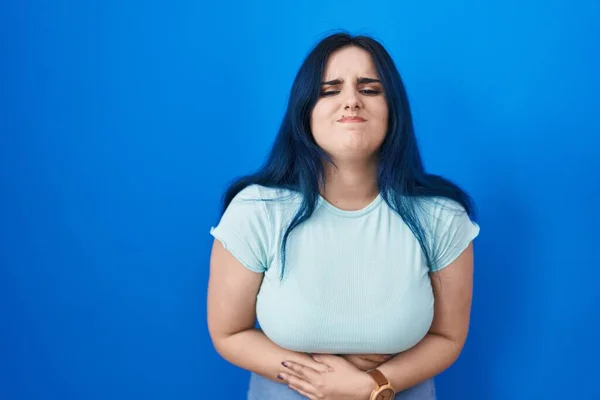 年轻的现代女孩 蓝头发 双手放在肚子上 站在蓝色的背景上 因为消化不良 痛苦不堪 疼痛的概念 — 图库照片