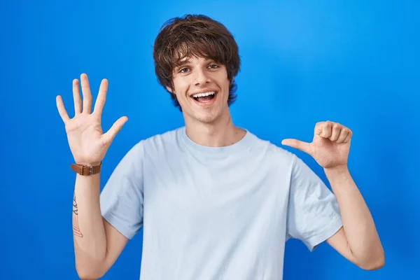 西班牙裔年轻人站在蓝色的背景上 带着自信和快乐的微笑 用六号手指指指着 — 图库照片