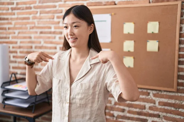 Chinese young woman working at the office doing presentation looking confident with smile on face, pointing oneself with fingers proud and happy.