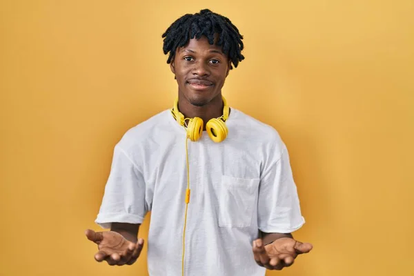 stock image Young african man with dreadlocks standing over yellow background clueless and confused with open arms, no idea concept. 