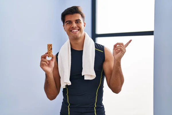 Hispanic man eating protein bar as healthy energy snack smiling happy pointing with hand and finger to the side