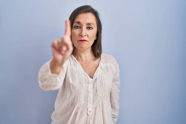 Orta Yaşlı Latin Bir Kadın Mavi Arka Planda Durup Parmağını — Stok fotoğraf