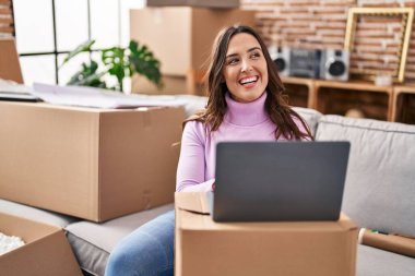 Young hispanic woman smiling confident using laptop at new house
