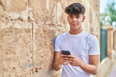 Young hispanic teenager smiling confident using smartphone at street