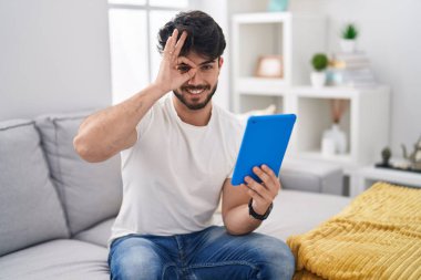 Sakallı İspanyol bir adam kanepeye oturmuş gülümsüyor ve mutlu yüzüyle parmaklarının arasından bakıyor.. 