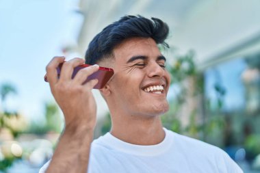 Genç İspanyol gülen adam caddedeki akıllı telefondan kendine güvenen bir sesli mesaj dinliyor.