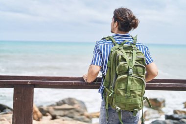 Sırt çantalı genç İspanyol turist, deniz kenarındaki balyalara yaslanıyor.