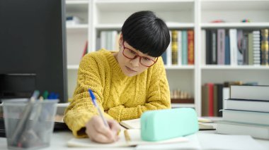 Kütüphanede okuyan, not defterine yazan Çinli genç bir kız öğrenci.