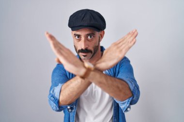 Sakallı İspanyol bir adam, izole edilmiş arka planda duruyor. Reddedilmiş yüz ifadesi, kollarını kavuşturup negatif işaret veriyor. 