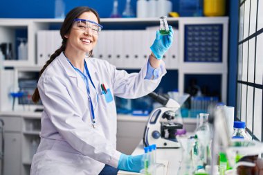 Young woman scientist writing on notebook holding test tube at laboratory