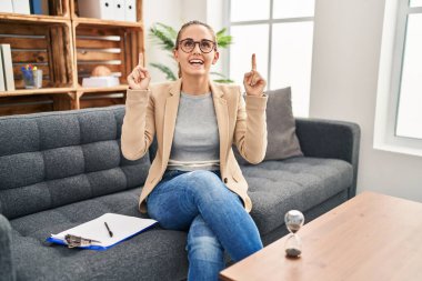 Muayenehanede çalışan genç bir kadın şaşırmış, şaşırmış ve parmaklarıyla işaret ediyor ve kollarını kaldırıyordu.. 