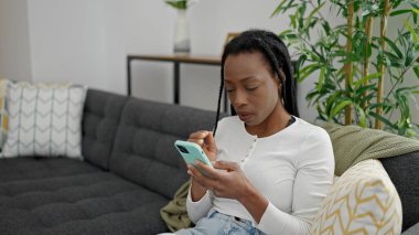 Evdeki koltukta oturan Afro-Amerikan kadın akıllı telefon kullanıyor