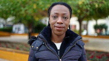 Afro-Amerikalı kadın parkta kendinden emin bir şekilde gülümsüyor.