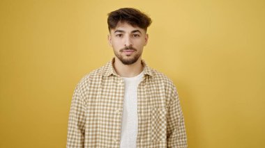 İzole edilmiş sarı arka planda gevşek bir ifadeyle duran genç bir Arap.