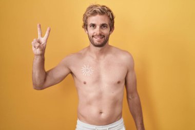 Beyaz adam üstsüz, güneş kremi sürmüş ve iki numaralı parmaklarıyla işaret ederken kendinden emin ve mutlu bir şekilde gülümsüyor.. 