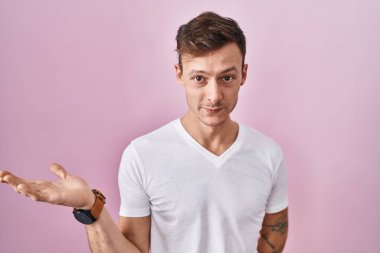 Pembe arka planda duran beyaz adam mutlu bir şekilde sunum yapıyor ve avuç içi kameraya bakıyor.. 