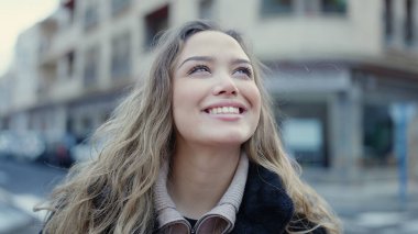Young beautiful hispanic woman smiling confident looking to the sky at street