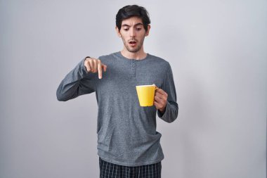 Pijama giyen, kahve içen, parmaklarıyla işaret eden, reklamını yapan, şaşırmış yüzlü ve ağzı açık genç İspanyol bir adam. 