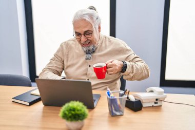 Middle age grey-haired man business worker using laptop drinking coffee at office