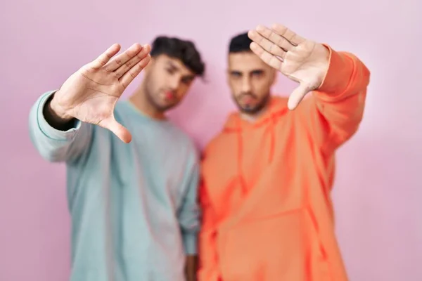 stock image Young hispanic gay couple standing over pink background doing frame using hands palms and fingers, camera perspective 