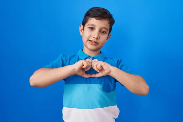 手でハートのシンボルの形をする愛の青の背景笑顔の上に立つ小さなヒスパニック系の少年 ロマンチックなコンセプト — ストック写真