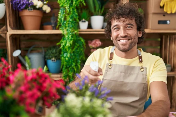 Young hispanic man florist using diffuser watering plant at flower shop
