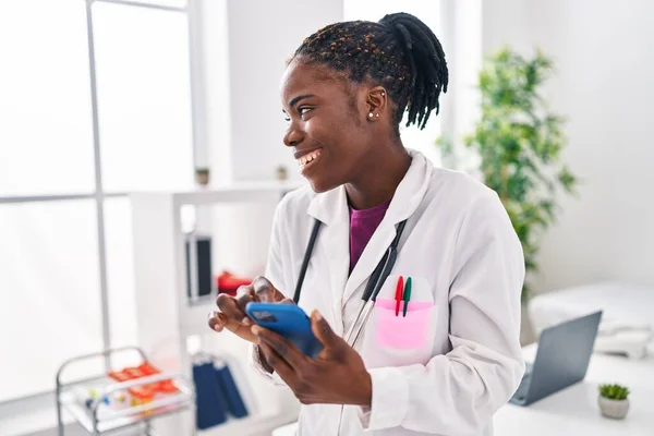 アフリカ系アメリカ人医師の制服を着た女性がクリニックでスマートフォンを使って — ストック写真
